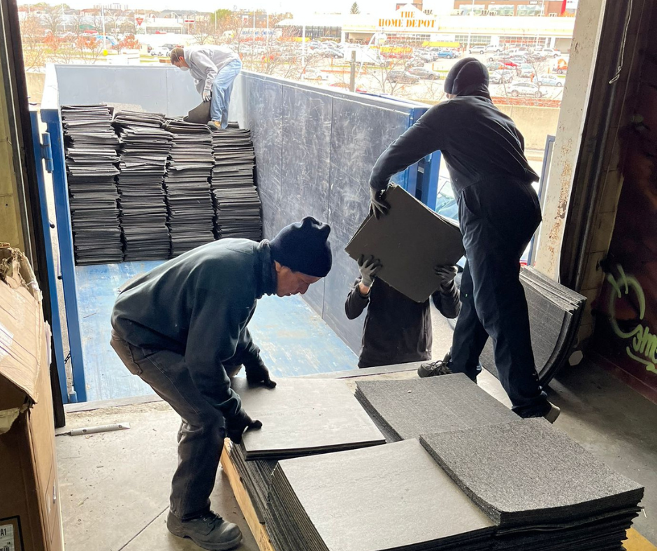 Three people moving cut carpet into a shipping container